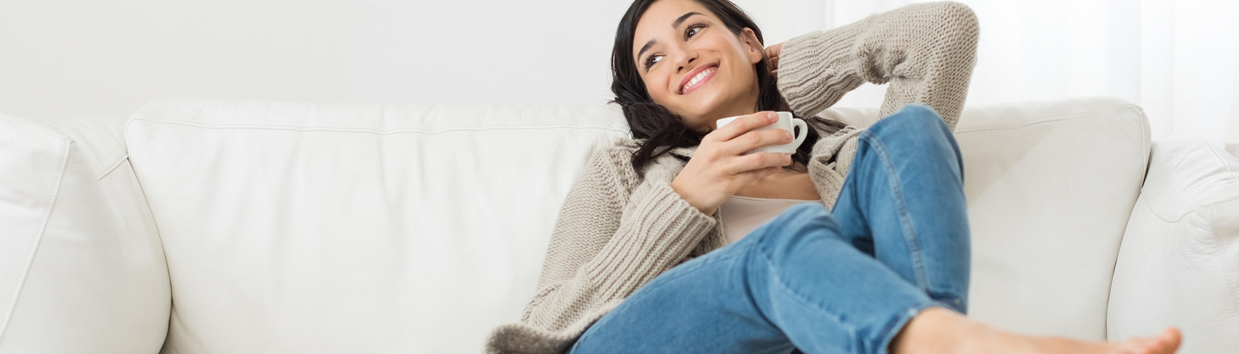 Eine Frau entspannt auf dem Sofa und trinkt einen Kaffee. Gemütlich warmes Zuhause dank Heizungen der Firma Haesler AG.